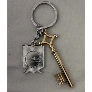 May include: A silver keychain with a gold-colored key and a silver emblem. The key has a diamond-shaped top and a detailed handle. The emblem has Japanese text and a circular design. The keychain ring is silver.