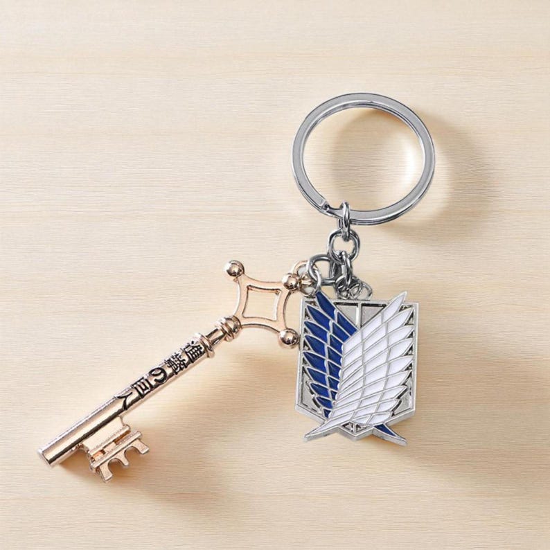 May include: A keychain featuring a gold-colored key with Japanese text and a silver-colored ring. The keychain also includes a pendant with a blue and white wing design.