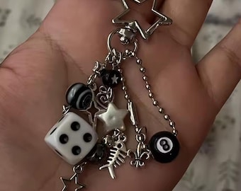 May include: A silver keychain with a star-shaped clasp and various charms. Charms include a white die with black dots, a black and white striped bead, a black eight ball, and star-shaped charms.
