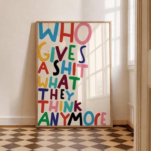 May include: A rectangular framed wall art piece featuring the text WHO GIVES A SHIT WHAT THEY THINK ANYMORE in large, hand-drawn style letters. The letters are rendered in a variety of vibrant colours including blue, red, pink, yellow, green, and black.