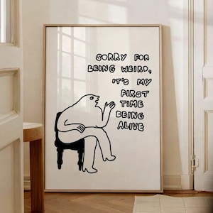 May include: A framed art print with a minimalist illustration of a seated figure. The black and white artwork features the text "SORRY FOR BEING WEIRD, IT'S MY FIRST TIME BEING ALIVE."