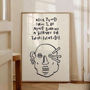 May include: A framed art print with a minimalist black and white design. The artwork features a stylized human head illustration and the handwritten text: "ADULTHOOD SEEMS TO BE ABOUT BUILDING A TOLERANCE FOR THINGS INEVITABLE."