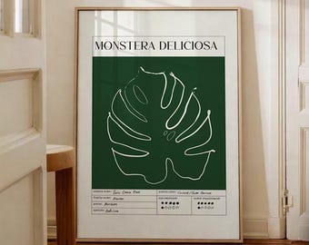 May include: A framed art print featuring a white line drawing of a Monstera leaf on a dark green background. The text "MONSTERA DELICIOSA" is at the top, with additional text and rating indicators at the bottom. The frame is gold.