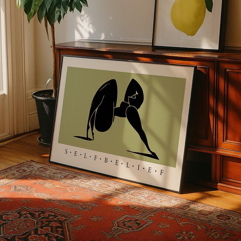 May include: A framed rectangular wall art print featuring a sage green background with a black abstract silhouette of a figure in a bent pose. The text S&middot;E&middot;L&middot;F&middot;B&middot;E&middot;L&middot;I&middot;E&middot;F is printed in black capital letters at the bottom of the print.