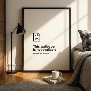 May include: A framed print with a black border displays a pixelated sad face icon and the text "This wallpaper is not available." A black desk lamp and a white mug are visible.