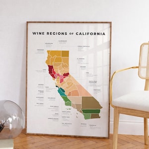 May include: A framed print titled "Wine Regions of California" displays a colorful map of California, highlighting various wine-producing regions. The map is in a wooden frame, with a chair and a decorative glass sphere in the background.