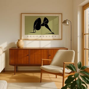 May include: A framed horizontal wall art print featuring a stylized black silhouette of a person in a yoga pose against a muted olive green background, with the text S E L F B E L I E F printed in black capital letters centered below the figure.