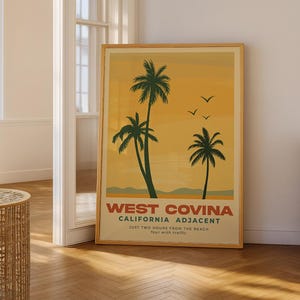 May include: A framed poster featuring a vintage travel design. The artwork showcases three palm trees in silhouette against a yellow and orange gradient sky. Text at the bottom reads "West Covina, California Adjacent".