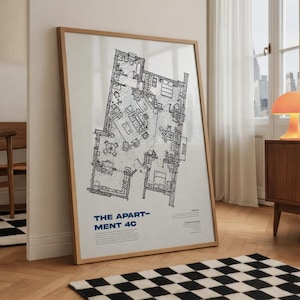 Op de afbeelding: Een ingelijste architectonische plattegrond van een appartement, met gedetailleerde lijntekeningen van kamers en meubels. De tekst "THE APARTMENT 4C" staat in het blauw onderaan. De lijst is lichtbruin van kleur en de print leunt tegen een muur.