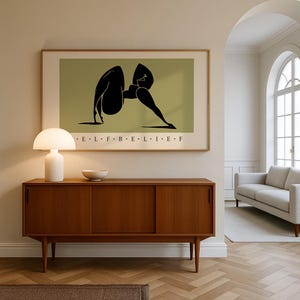 May include: A framed horizontal wall art print featuring a black abstract silhouette of a figure in a yoga pose against an olive green background. The text E L F B E L I E F is printed in black capital letters centered below the illustration.