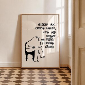 May include: A framed art print with a black and white illustration of a seated figure. The text reads "Sorry for being weird, it's my first time being alive." The artwork has a minimalist design and is suitable for home decor.