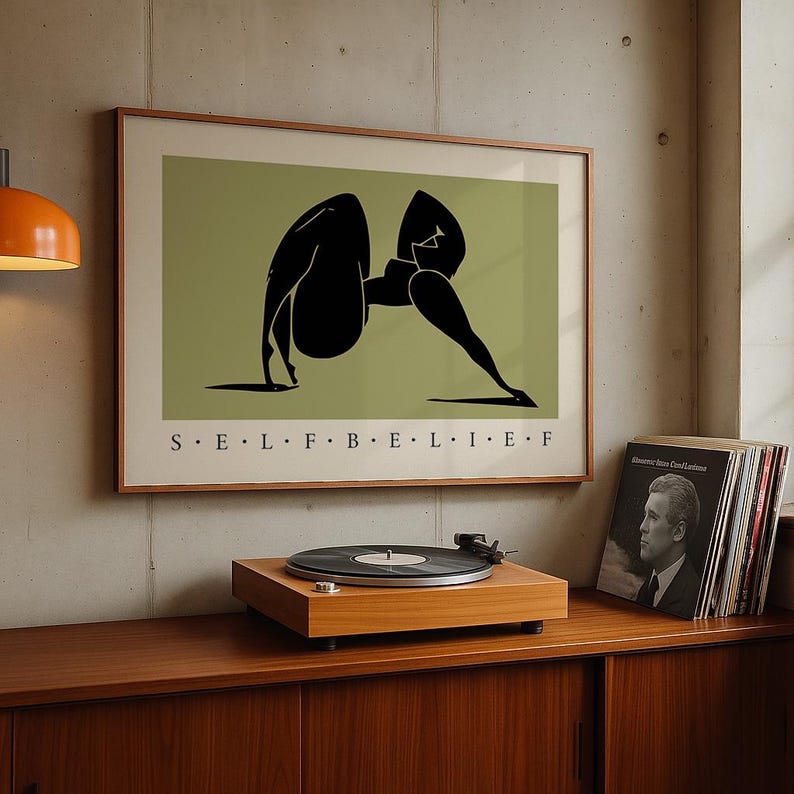 May include: A framed rectangular wall art print featuring a stylized black silhouette of a person in a yoga pose against a muted olive green background. The text S E L F B E L I E F is printed in black capital letters centered below the illustration.