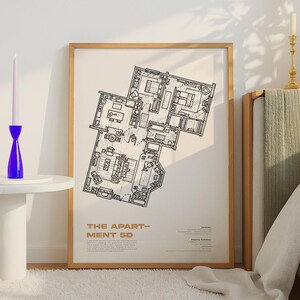 May include: A framed print featuring a detailed black and white floor plan labeled "THE APARTMENT 5D." The print is in a light wood frame and is displayed on a wall. A blue candle holder and candle are on a white table.