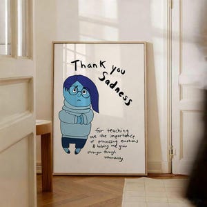 May include: A rectangular wall art print featuring a cartoon character with blue skin, dark blue hair, and round glasses, wearing a light blue turtleneck sweater. The text reads: Thank you Sadness for teaching me the importance of processing emotions & helping me grow stronger through vulnerability.