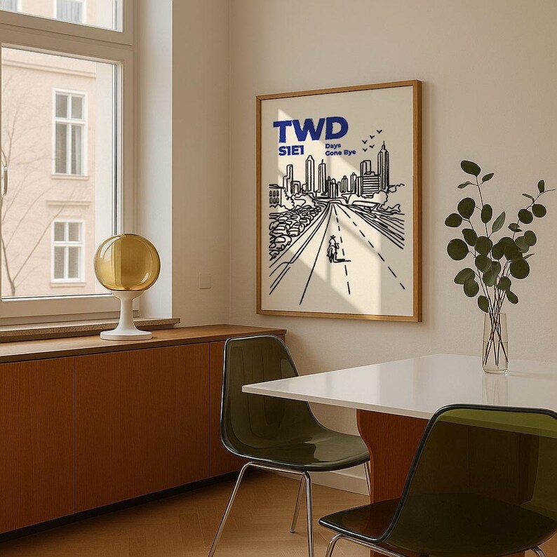 May include: A framed art print featuring a black and white illustration of a city street with a person walking down the road. The print has the text "TWD S1E1 Days Gone Bye" in blue. The artwork is displayed in a room with a window and a table.