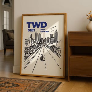 May include: Framed art print featuring a black and white illustration of a city skyline and a road with a lone figure. The print includes the text "TWD S1E1 Days Gone Bye" in blue, set against a cream background, framed in a wooden frame.