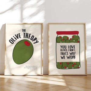 May include: Two framed art prints with olive-themed designs. One features a large green olive with the text "THE OLIVE THEORY". The other shows a jar of olives with the text "YOU LOVE OLIVES. I DON'T. THAT'S WHY WE WORK".