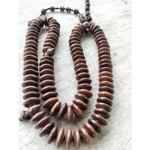 May include: A necklace made of dark brown wooden beads. The beads are disc-shaped and strung together, creating a layered effect. The necklace has a natural, earthy aesthetic, suitable for casual wear. The beads are measured in centimetres.
