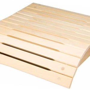 Può includere: Una panca per sauna in legno chiaro con una forma curva e un design a doghe. La panca ha una finitura naturale ed è realizzata in legno massello.
