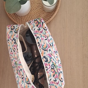May include: A rectangular zippered toiletry bag featuring a colorful abstract animal print pattern in shades of pink, orange, teal, and black. The open bag contains a dark brown hair dryer and a black pump bottle inside a cream-colored interior.