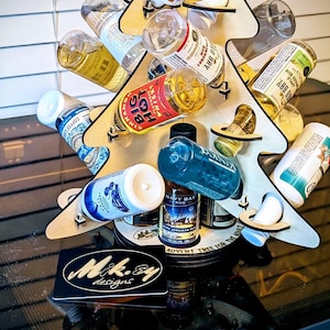 May include: A wooden advent calendar in the shape of a Christmas tree, holding various miniature liquor bottles. The tree is made of light-colored wood and has cutouts to hold the bottles. The base has a black label with the text "Mik.sy designs".