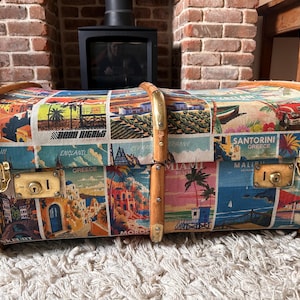 May include: A vintage travel trunk with a collage of travel destinations. The trunk has brass hardware, wooden accents, and a lock. Destinations include Miami, Santorini, and England.
