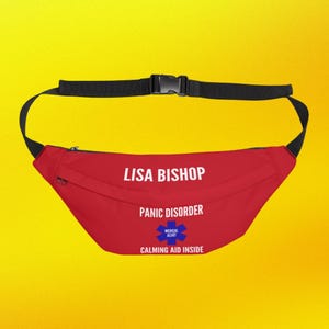 Może przedstawiać: Czerwona nerka z regulowanym czarnym paskiem i klamrą. Tekst "LISA BISHOP" jest wydrukowany na biało, wraz z "PANIC DISORDER" i "MEDICAL ALERT" z niebieskim symbolem gwiazdy oraz "CALMING AID INSIDE".