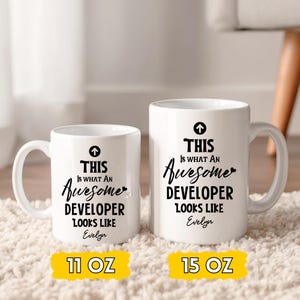Op de afbeelding: Twee witte keramische mokken met zwarte tekst: "THIS IS WHAT AN Awesome DEVELOPER LOOKS LIKE Evelyn." E&eacute;n mok is 325 ml, de andere is 444 ml. Beide hebben een zwarte pijl boven de tekst.