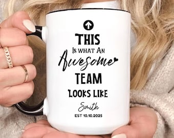 May include: White ceramic mug with black handle and rim, featuring the text "THIS Is WHAT AN Awesome TEAM LOOKS LIKE Smith EST 10.10.2025" in black. The mug is held by a person.