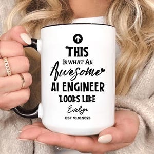 May include: White ceramic mug with a black handle and rim. The mug features the text "THIS Is WHAT AN Awesome AI ENGINEER LOOKS LIKE Evelyn EST 10.10.2025" in black font. The mug is held by a person.