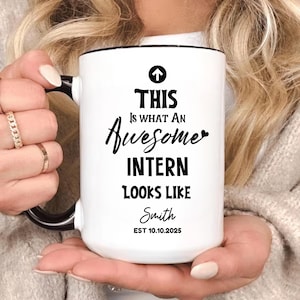 May include: White ceramic mug with black handle and rim. The mug features the text "THIS IS WHAT AN Awesome INTERN LOOKS LIKE" in black script. Below the text is the name "Smith" and the date "EST 10.10.2025".