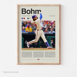 May include: A baseball poster featuring a player in a red, white, and blue uniform swinging a bat. The poster has a white background with the player's name "Bohm" in black text and the text "Philadelphia Phillies" and "Third Baseman" in smaller black text. The poster also includes a small American flag.