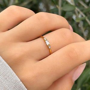 May include: A delicate gold ring with three small, clear baguette-shaped stones set in a thin band.