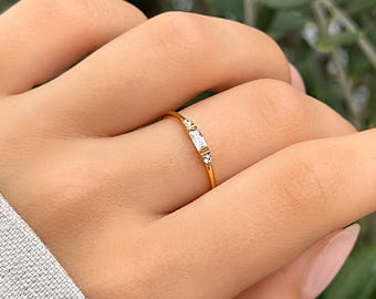 May include: A delicate gold ring with three small, clear baguette-shaped stones set in a thin band.