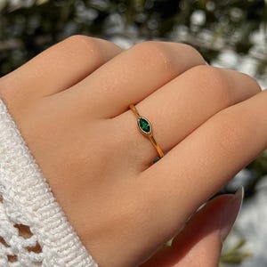 Può includere: Un anello d'oro con una piccola pietra preziosa verde di forma ovale.