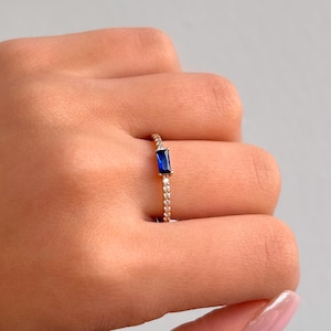 May include: A gold ring with a blue rectangular gemstone and small clear stones around the band.
