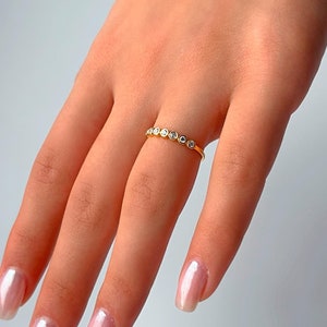 Könnte beinhalten: Ein goldener Ring mit einer Reihe kleiner, klarer Edelsteine. Der Ring befindet sich an einem Finger mit hellrosa Nagellack.