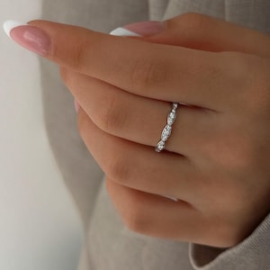 Peut inclure: Une délicate bague en argent avec une rangée de petites pierres précieuses claires serties dans un motif ondulé.