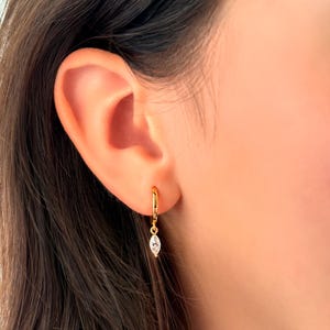 Può includere: Orecchini a cerchio dorati con una pietra trasparente a forma di marquise pendente.