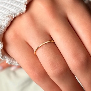 Könnte beinhalten: Ein dünner goldener Ring mit einem gedrehten Design.