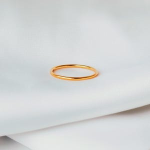 Può includere: Un semplice anello a fascia d'oro su uno sfondo di tessuto bianco.