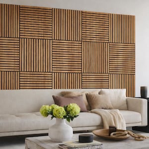 Puede incluir: Un salón moderno con un sofá de color claro, cojines decorativos y una pared de acento de madera. Un jarrón blanco contiene flores verdes y una mesa de centro de madera está frente al sofá.