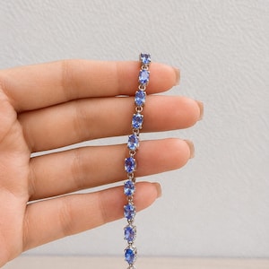 Può includere: Un bracciale tennis color argento caratterizzato da una serie di pietre preziose azzurre dal taglio ovale, incastonate in una delicata catena di metallo. Il bracciale presenta una disposizione uniforme di undici pietre, fissate da quattro griffe.