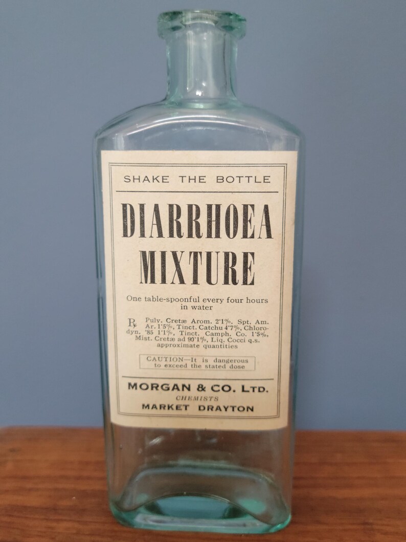 Peut inclure: Une bouteille de m&eacute;dicament en verre bleu clair transparent avec un corps rectangulaire et un col court. Une &eacute;tiquette en papier blanc est fix&eacute;e sur le devant, avec un texte noir indiquant SHAKE THE BOTTLE, DIARRHOEA MIXTURE, des instructions de dosage, des ingr&eacute;dients et MORGAN & CO. LTD. CHEMISTS MARKET DRAYTON.