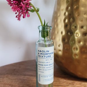 Peut inclure: Une bouteille d'apothicaire en verre transparent avec une &eacute;tiquette blanche portant l'inscription KAOLIN & MORPHINE MIXTURE, B.P.C. 1968, CONTENTS 200 ml. DOSE FOR ADULTS, Two 5 ml. spoonfuls to be taken three times a day in water. SHAKE THE BOTTLE.