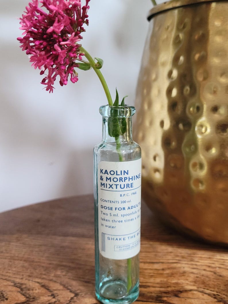 Peut inclure: Une bouteille d'apothicaire en verre transparent avec une &eacute;tiquette blanche portant l'inscription KAOLIN & MORPHINE MIXTURE, B.P.C. 1968, CONTENTS 200 ml. DOSE FOR ADULTS, Two 5 ml. spoonfuls to be taken three times a day in water. SHAKE THE BOTTLE.