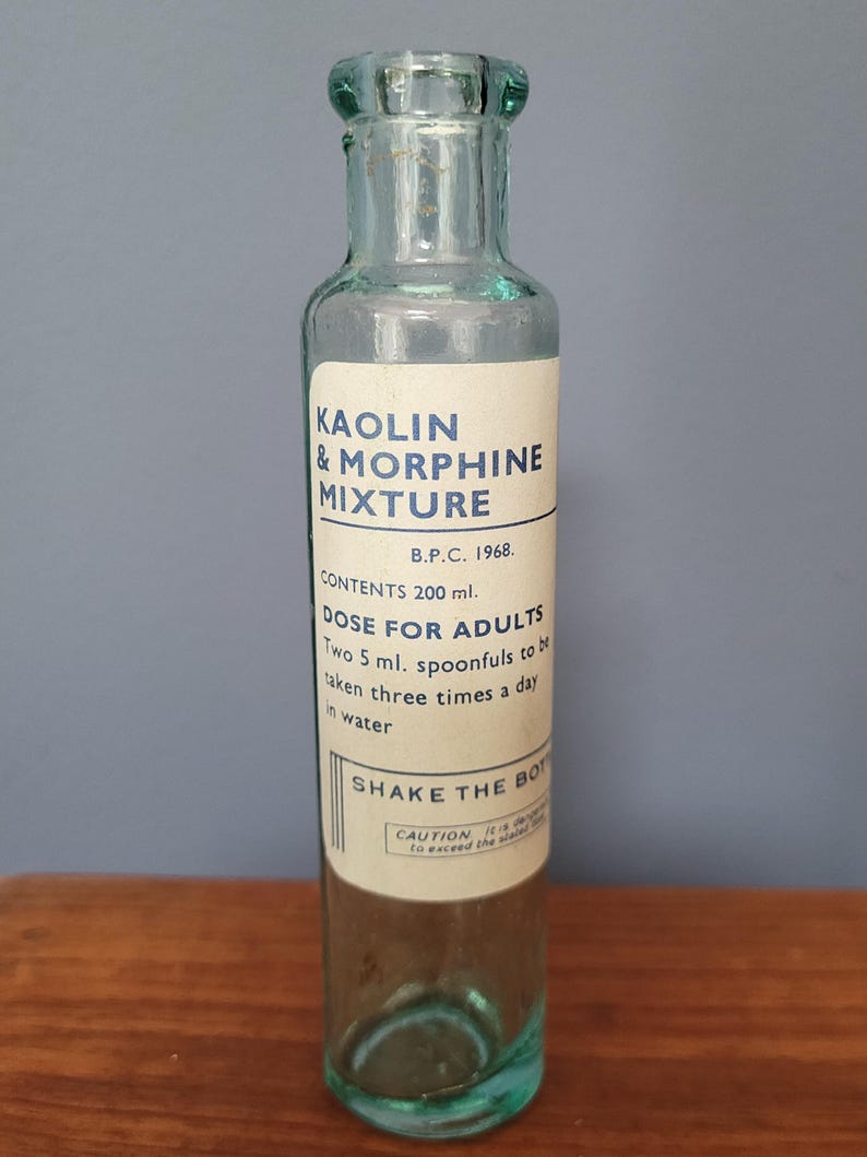 Peut inclure: Une bouteille de m&eacute;dicament en verre bleu clair transparent avec un corps cylindrique et un goulot &eacute;troit. L'&eacute;tiquette blanche porte le texte KAOLIN & MORPHINE MIXTURE, B.P.C. 1968, CONTENTS 200 ml, DOSE FOR ADULTS, SHAKE THE BOTTLE et CAUTION en bleu.