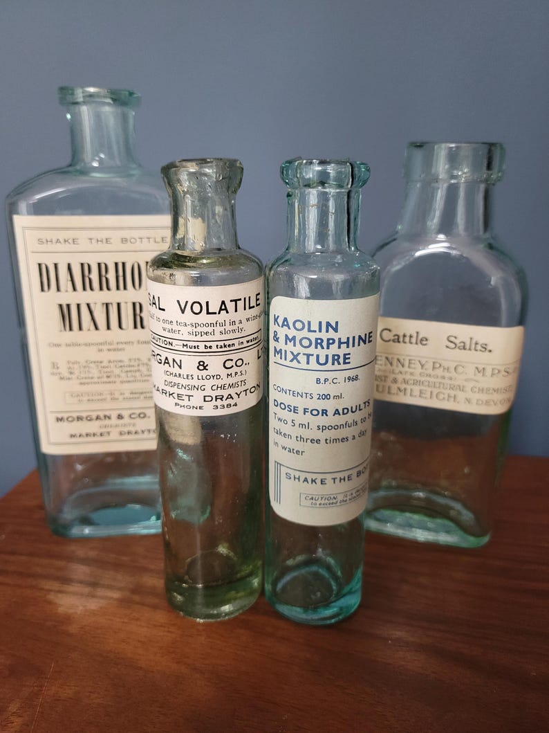 Peut inclure: Quatre flacons d'apothicaire vintage en verre transparent avec &eacute;tiquettes. Les &eacute;tiquettes portent des inscriptions telles que Diarrhoea Mixture, Sal Volatile, Kaolin & Morphine Mixture et Cattle Salts. Les flacons ont des formes vari&eacute;es, dont un de 200 ml.