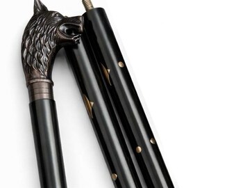 May include: Black walking cane with a wolf head handle. The handle is bronze-colored, and the cane has gold-colored accents. The cane is made of three sections that screw together. The cane is designed for support and style.