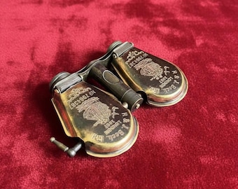May include: Antique brass opera glasses with a handle and engraved details. The glasses are marked "R & J Beck, London 1897" and feature a serial number. The design includes a decorative crest and a small adjustment lever.